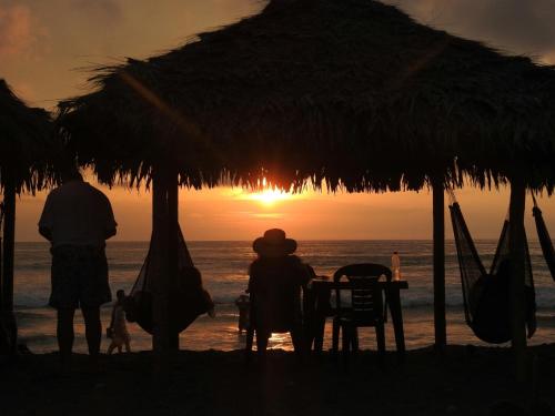 two people sitting at a table on the beach at sunset at Wipeout Cabaña Restaurant in Las Tunas
