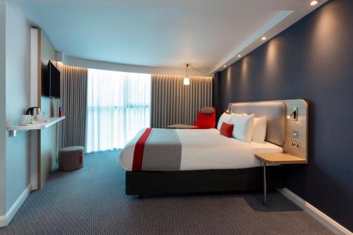ロンドンにあるホリデイ イン エクスプレス パーク ロイヤルのベッドと赤い椅子が備わるホテルルームです。