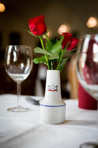 a vase with red roses on a table with a glass at Hotel Štekl in Hluboká nad Vltavou