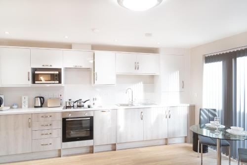 a kitchen with white cabinets and a glass table at Citystay - Hinton House in Cambridge