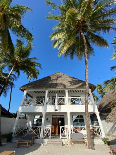 a white house on the beach with palm trees at The African Paradise Beach Hotel in Bwejuu