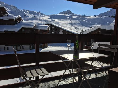 - une table et deux verres à vin sur un balcon avec des montagnes enneigées dans l'établissement DUPLEX 6P A BELLE-PLAGNE (2050 m), SKIS AUX PIEDS, EN PLEIN CŒURS DE LA STATION RESIDENCE LE BERYL., à Belle Plagne