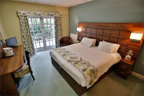 a bedroom with a bed and a desk and a window at Quorn Grange Hotel in Loughborough