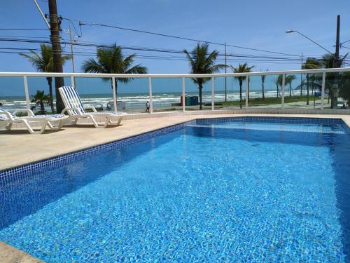 a swimming pool with chairs and the ocean in the background at Apartamento Cheryl in Praia Grande