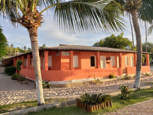 an orange house with palm trees in front of it at Pousada Grão de Areia Beira Mar in Mangue Sêco