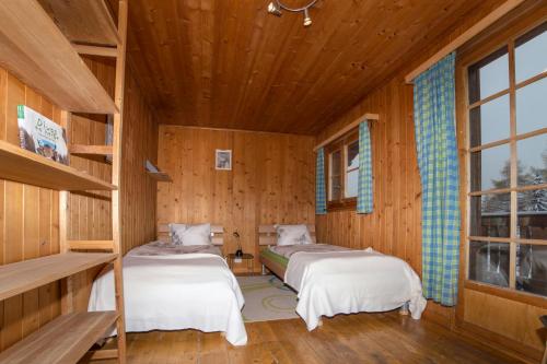 two beds in a room with wooden walls at le castor in Morgins