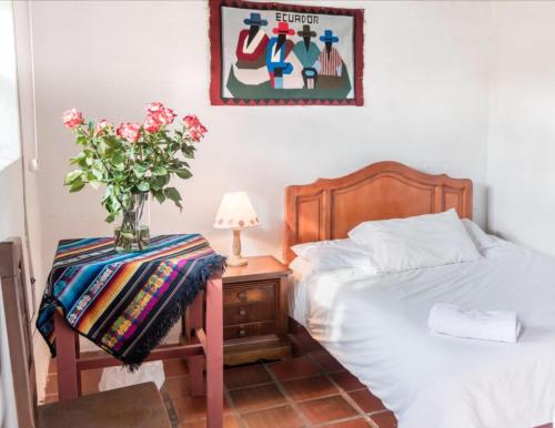 a bedroom with a bed and a table with a vase of flowers at Hostería Colibri Aeropuerto in Tababela