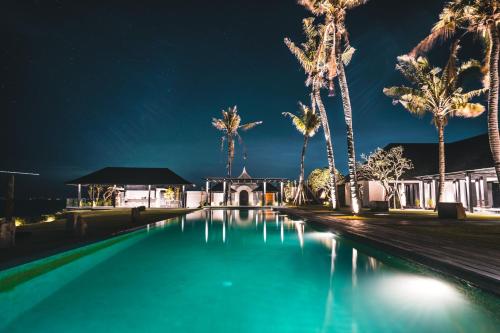 una piscina di fronte a una casa con palme di Detox and Spa Package - The Istana a Uluwatu