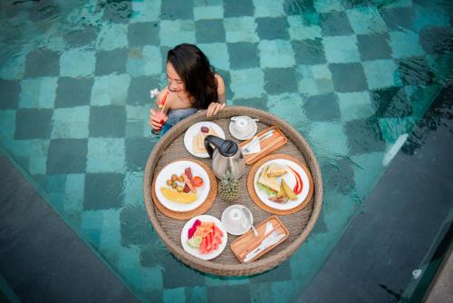 una donna seduta in piscina con un tavolo di cibo di Auma Villa by Prasi ad Ubud
