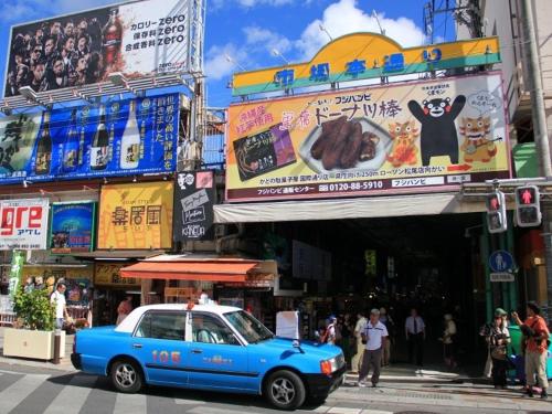 a blue car driving down a street in a city at Living Inn Asahibashiekimae Premier in Naha