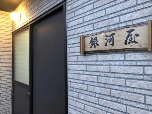 ein Schild an einer Ziegelmauer neben einer Tür in der Unterkunft GINGAYA in Iwataki