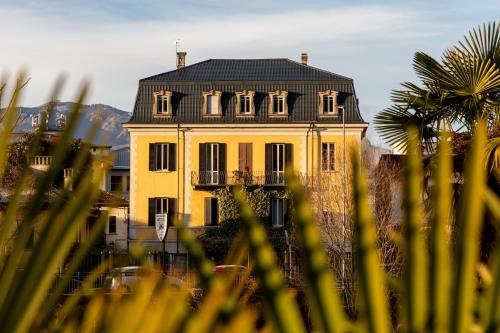 una casa gialla con tetto nero e palma di Hotel Casa Camilla a Verbania
