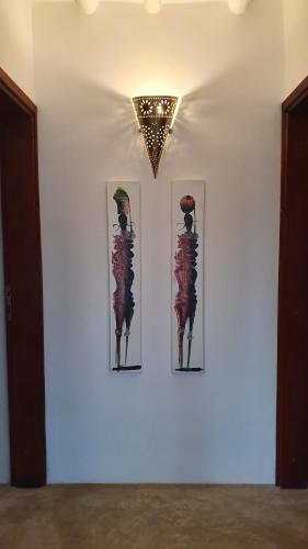 three pictures on a white wall with a chandelier at MOYO apartment in Pwani Mchangani