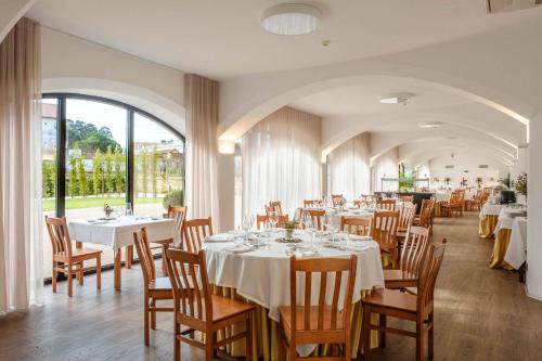 a dining room with white tables and chairs and windows at SDivine Fatima Hotel, Congress & Spirituality in Fátima