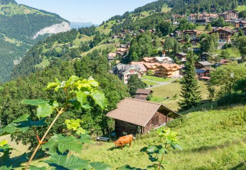 a cow standing in a field in front of a village at Panoramapark Soleil Chalet B in Wengen
