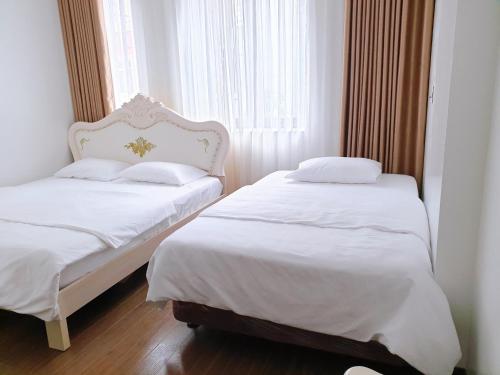 two beds in a room with white sheets and a window at The Peninsula Haiphong in Hai Phong