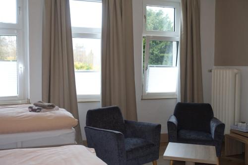 a hotel room with two chairs and a bed and windows at Gasthof & Restaurant "Am Kreuz" in Essen