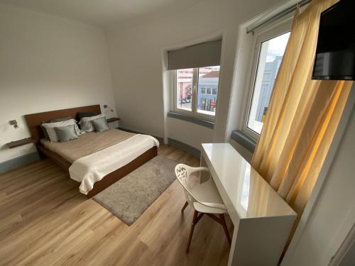 a bedroom with a bed and a desk and two windows at Guest House Infante Dom Henrique in Coimbra