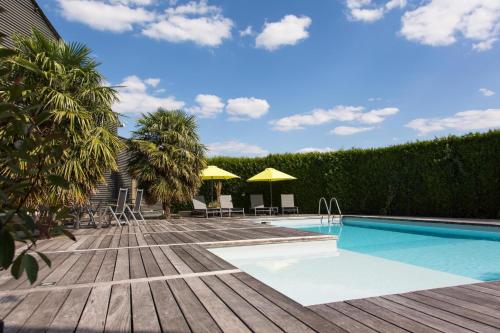 una piscina con sillas y sombrillas en una terraza de madera en Gîtes de La Vesée, en La Chapelle dʼArmentières