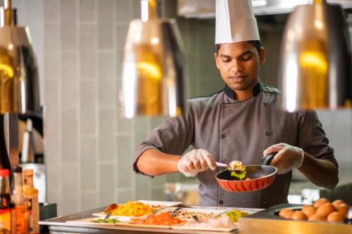 a man in a chefs hat preparing food in a kitchen at Holiday Inn AlSeeb Muscat, an IHG Hotel in Muscat