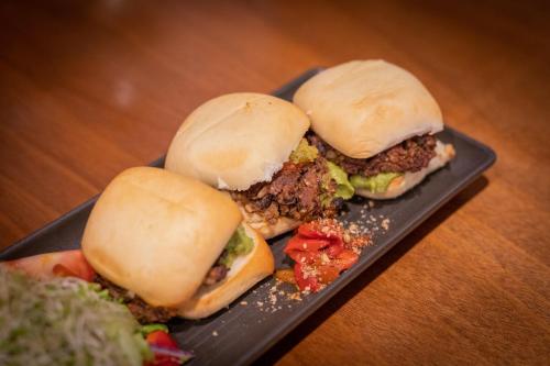 two pulled pork sandwiches on a black plate with vegetables at Beachfront Hotel Hokitika in Hokitika