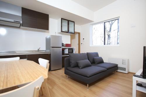 sala de estar con sofá negro y cocina en Apartments Hakuba, en Hakuba