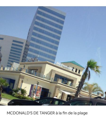 a building with a palm tree in front of a tall building at TANGER/ASILAH: APPART 50m2 FACE MER ET PISCINES, 5 PLACES, TOUT ÉQUIPÉ+WIFI+CLIM in Briech
