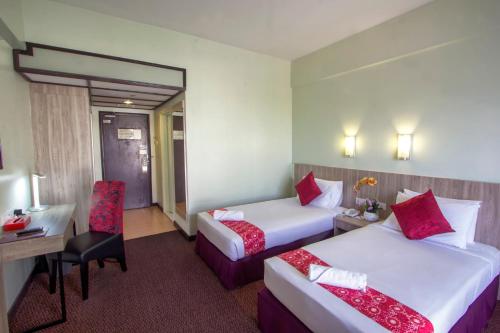 a hotel room with two beds and a desk and a chair at Hotel Grand Continental Langkawi in Kuah