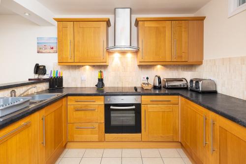 a kitchen with wooden cabinets and a stove top oven at West Beach - Holiday Apartments in Westward Ho