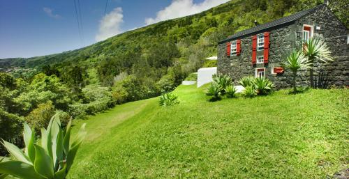 a stone house on a grassy hill with a mountain at Casas de Incensos - TER -TA in Pontas Negras