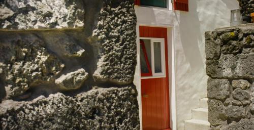 a building with a red door and a stone wall at Casas de Incensos - TER -TA in Pontas Negras