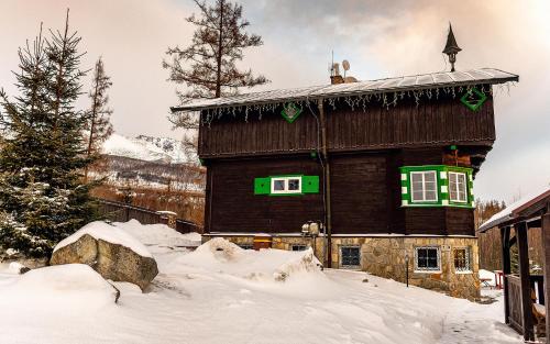 a large wooden building with green windows in the snow at Danielov dom in Vysoké Tatry