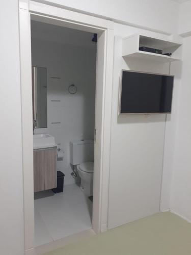 a bathroom with a toilet and a tv on a wall at Residencial Atalanta in Bombinhas