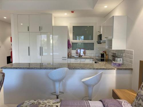 a kitchen with white cabinets and two stools at Purple Lily Studio Hawana Lagoons Salalah in Salalah