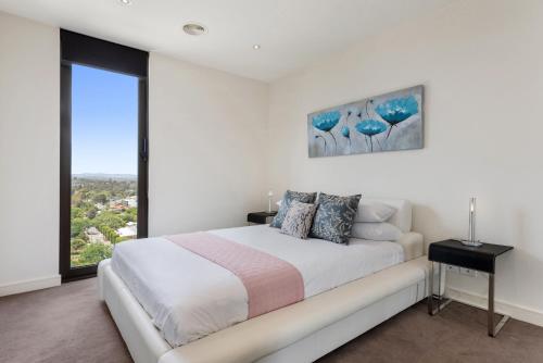 Un dormitorio blanco con una cama grande y una ventana en Ivanhoe Gem - Walk to Shops, Station & Great Views en Melbourne