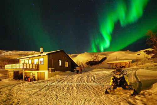 a person sitting on a snowmobile in the snow under the aurora at Rivdnji Holiday Home Smørfjord in Russenes