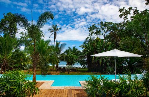 uma piscina de resort com um guarda-sol e palmeiras em Le Cameleon Boutique Hotel em Puerto Viejo