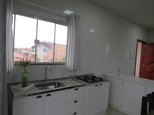 a white kitchen with a sink and a window at Residencial Coração do Mar in Palhoça