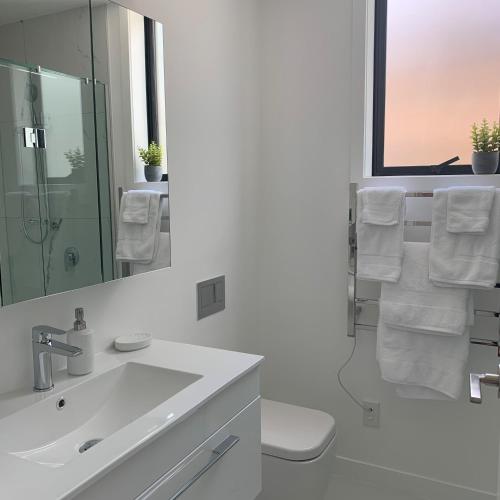a white bathroom with a sink and a mirror at De la Plage Residences in Orewa