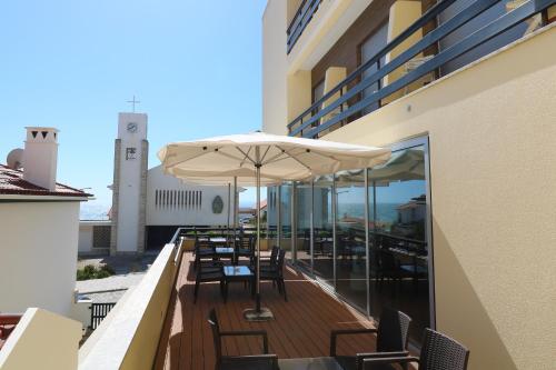 a balcony with chairs and an umbrella on a building at Hotel Miramar - São Pedro de Moel in São Pedro de Moel