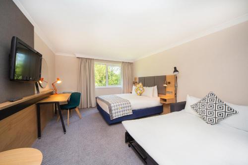 a hotel room with two beds and a desk and a tv at Holiday Inn Reading South M4 Jct 11, an IHG Hotel in Reading