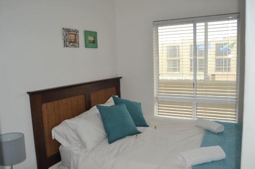 a white bed with blue pillows and a window at Lagoon Beach Neptune Isle Cape Town in Cape Town