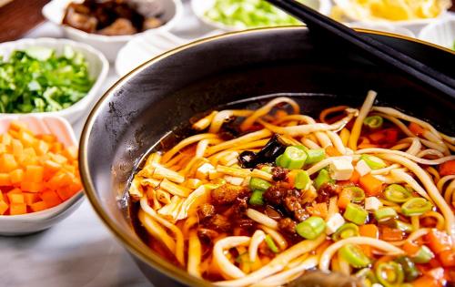 a bowl of food with noodles and vegetables on a table at Vignette Collection Haikou Yatter Hotel by IHG in Haikou