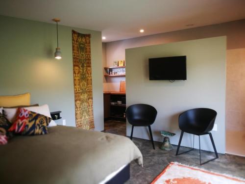 a bedroom with a bed and two chairs and a tv at Studio 40 in Coromandel Town