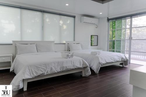 2 camas num quarto com paredes e janelas brancas em 3BU Hostel La Union em São Fernando