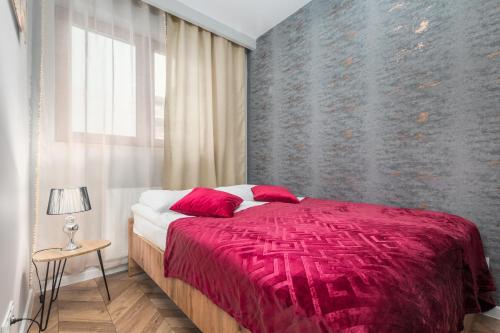 - une chambre avec un lit doté d'une couverture rouge et d'une fenêtre dans l'établissement Apartments Warsaw Markowska by Renters, à Varsovie