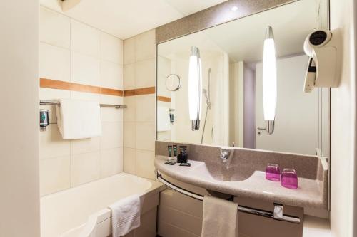 ein Badezimmer mit einem Waschbecken, einer Badewanne und einem Waschbecken in der Unterkunft Novotel Düsseldorf City West in Düsseldorf