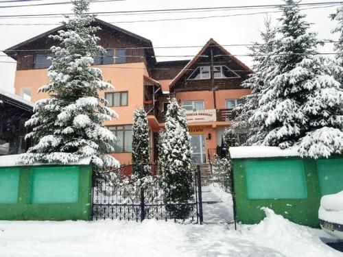 a house with snow covered trees in front of a fence at Pensiunea Agroturistică Piscul Soarelui in Cîmpulung