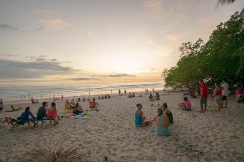a group of people sitting on the beach at sunset at Fuego Lodge in Santa Teresa Beach