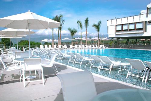 a pool with white chairs and umbrellas next to a building at Club Campestre De Bucaramanga in Bucaramanga